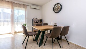 A dining area with a wooden table, four chairs, a wall clock, and a bookshelf with a 'HOME' sign. - Apartment Beleca (Podstrana)