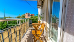 A balcony with a table and chairs, a potted plant, and a view of buildings and greenery. - Apartment Beleca (Podstrana)