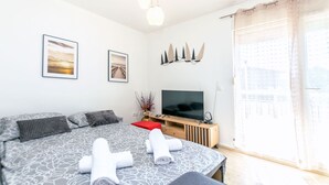 A modern bedroom with a large bed, a flat-screen TV, and a large window with sheer curtains. - Apartment Beleca (Podstrana)