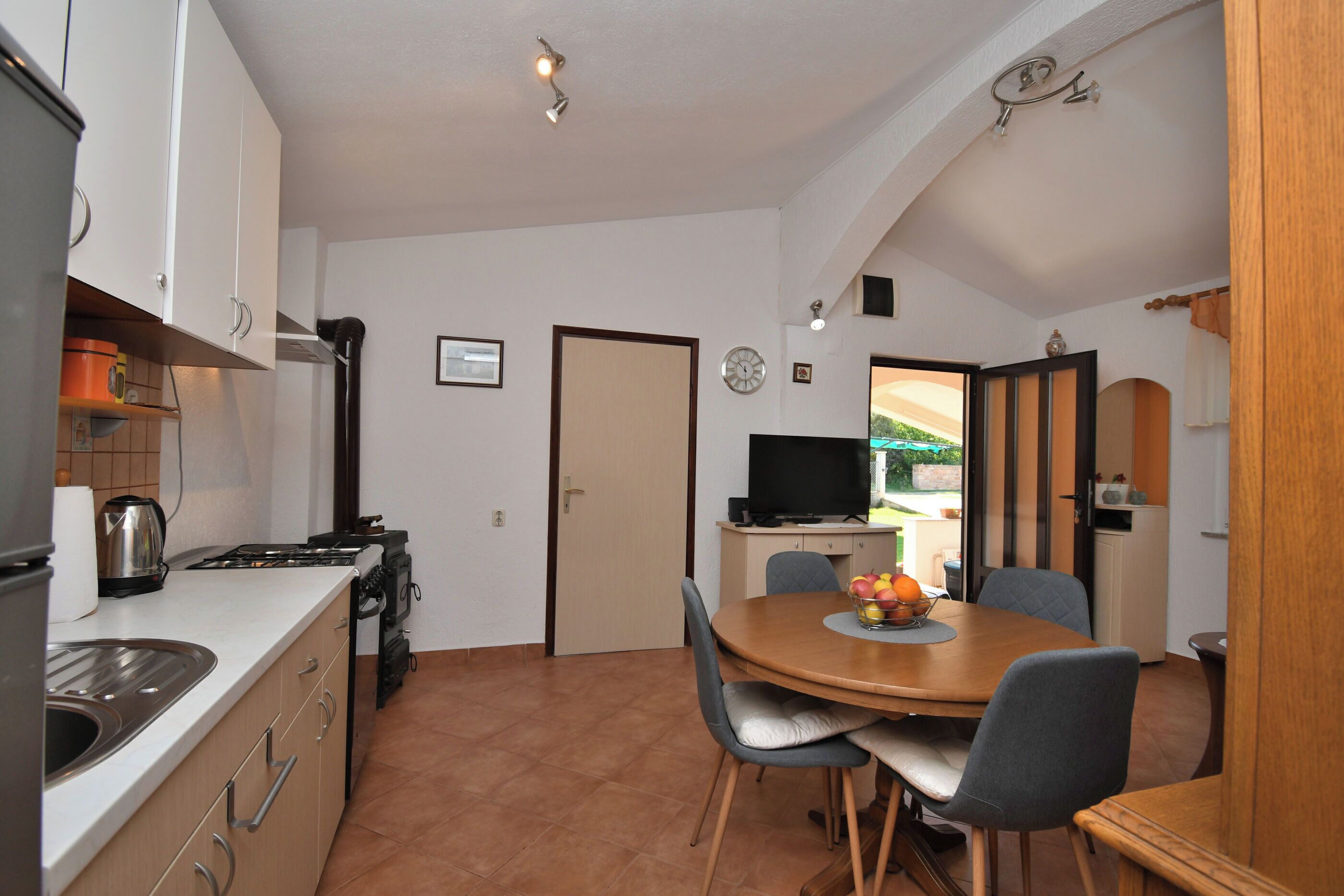 Una cucina compatta con elettrodomestici moderni, un'area pranzo con un tavolo rotondo e sedie, e una televisione sullo sfondo.