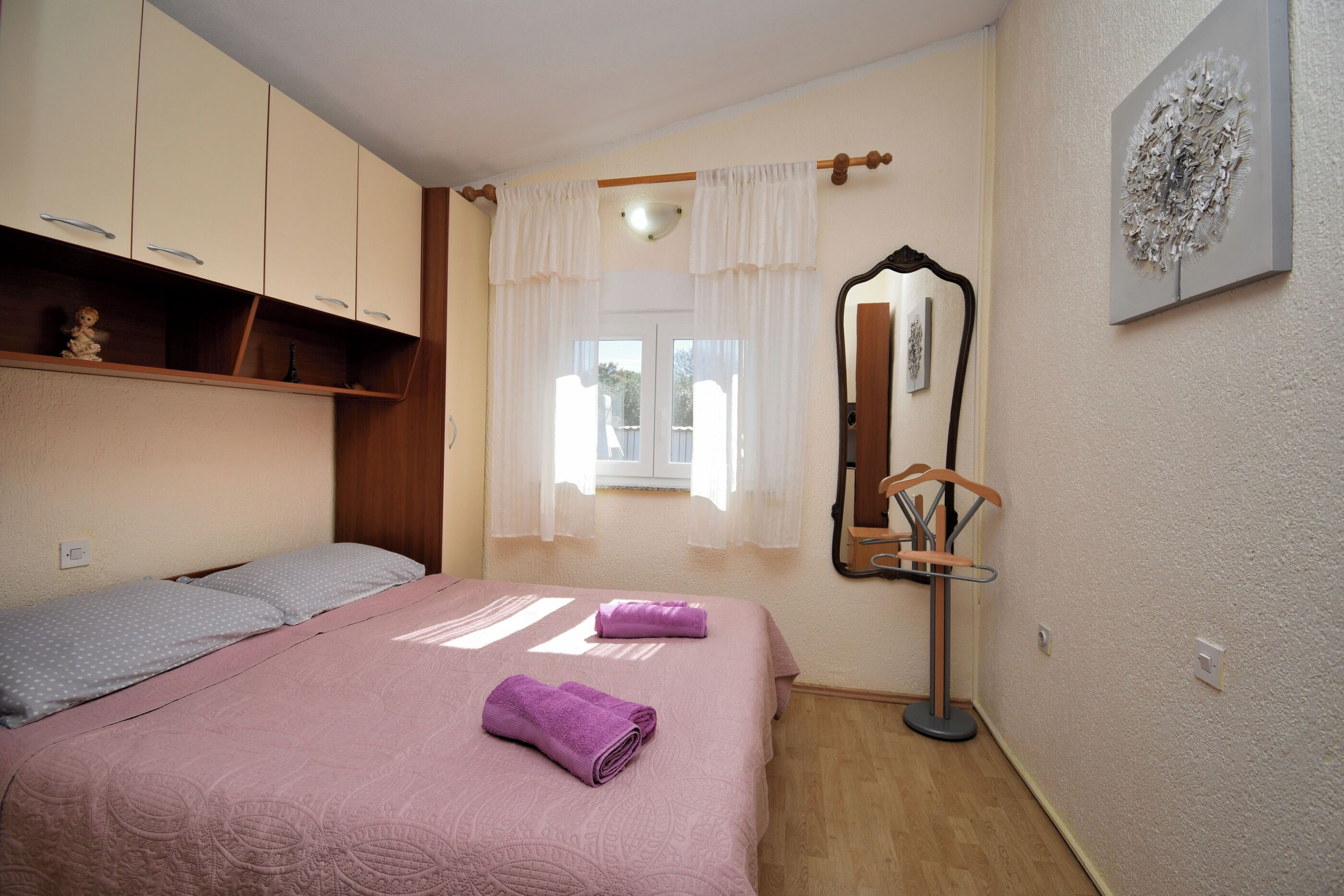 Une chambre à coucher avec un lit, une armoire, un miroir et une fenêtre avec des rideaux.