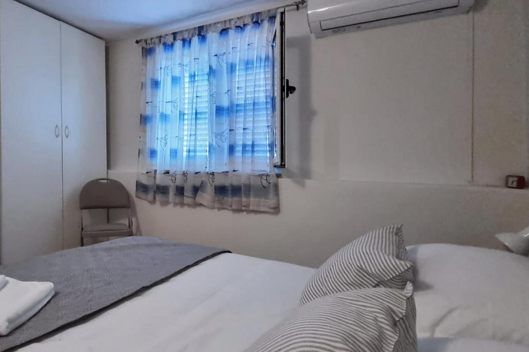 A bedroom with a bed, a chair, a wardrobe, and a window with curtains.