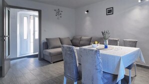 A modern dining area with a table set for four, a sofa, and a door leading to a bright room. - House Zlatni Otok (Sibenik)