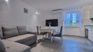 A modern living room with a grey sofa, a dining table with chairs, a flat-screen TV, and a window with curtains. - House Zlatni Otok (Sibenik)