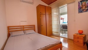 A bedroom with a wooden bed, a wardrobe, a small table with a lamp, and a sliding glass door leading to a balcony. - Apartment Mladen (Pakostane)