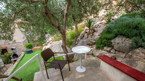 An outdoor patio with a round table and a chair, surrounded by greenery and a stone wall. - Apartment Mladen (Pakostane)