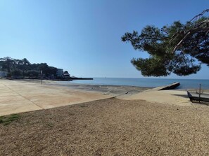 A beach with a concrete walkway, pebbles, and a large tree. - Apartments Vjera (Umag)