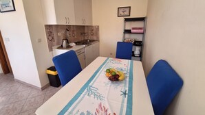 Un comedor con una mesa preparada para dos, una cocina al fondo y un cubo de basura a la izquierda.