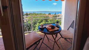 Un balcón con vista al mar, una mesa con una taza y un plato de comida, y una silla.