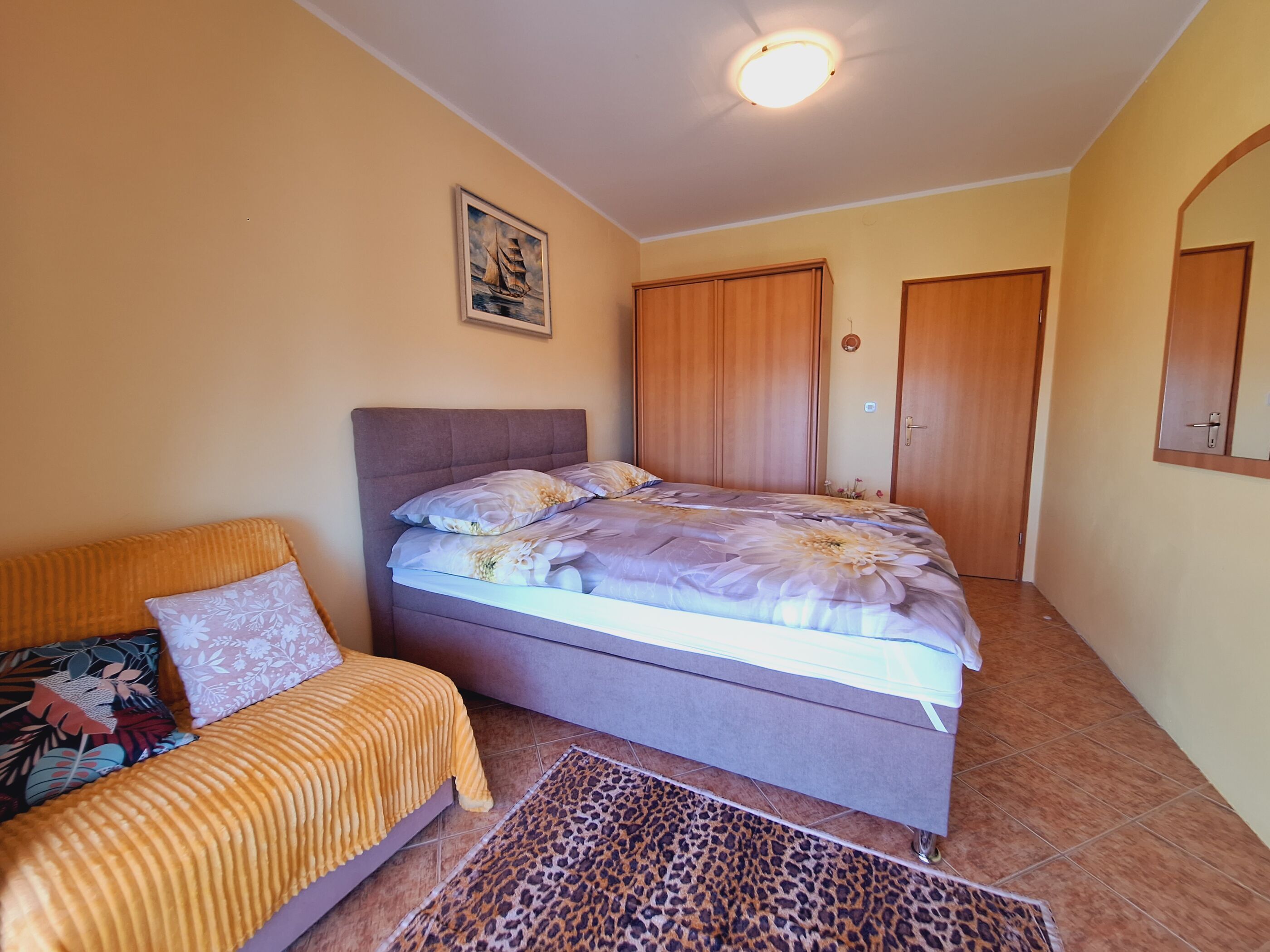 A bedroom with a bed, a sofa, a leopard print rug, and wooden wardrobes.