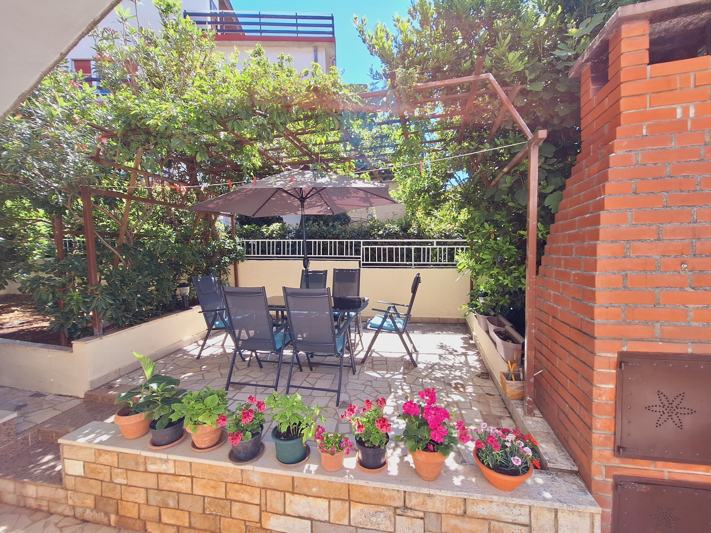 An outdoor patio with a table and chairs, surrounded by potted plants and a brick wall.