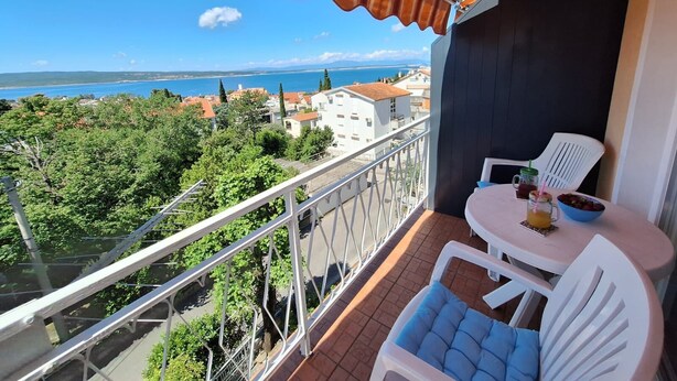 Un balcón con vista al mar, una mesa con sillas y una mesita con bebidas y aperitivos.