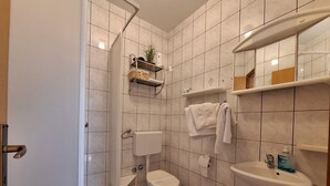 Un baño con ducha, inodoro, lavabo y repisas con artículos de aseo.