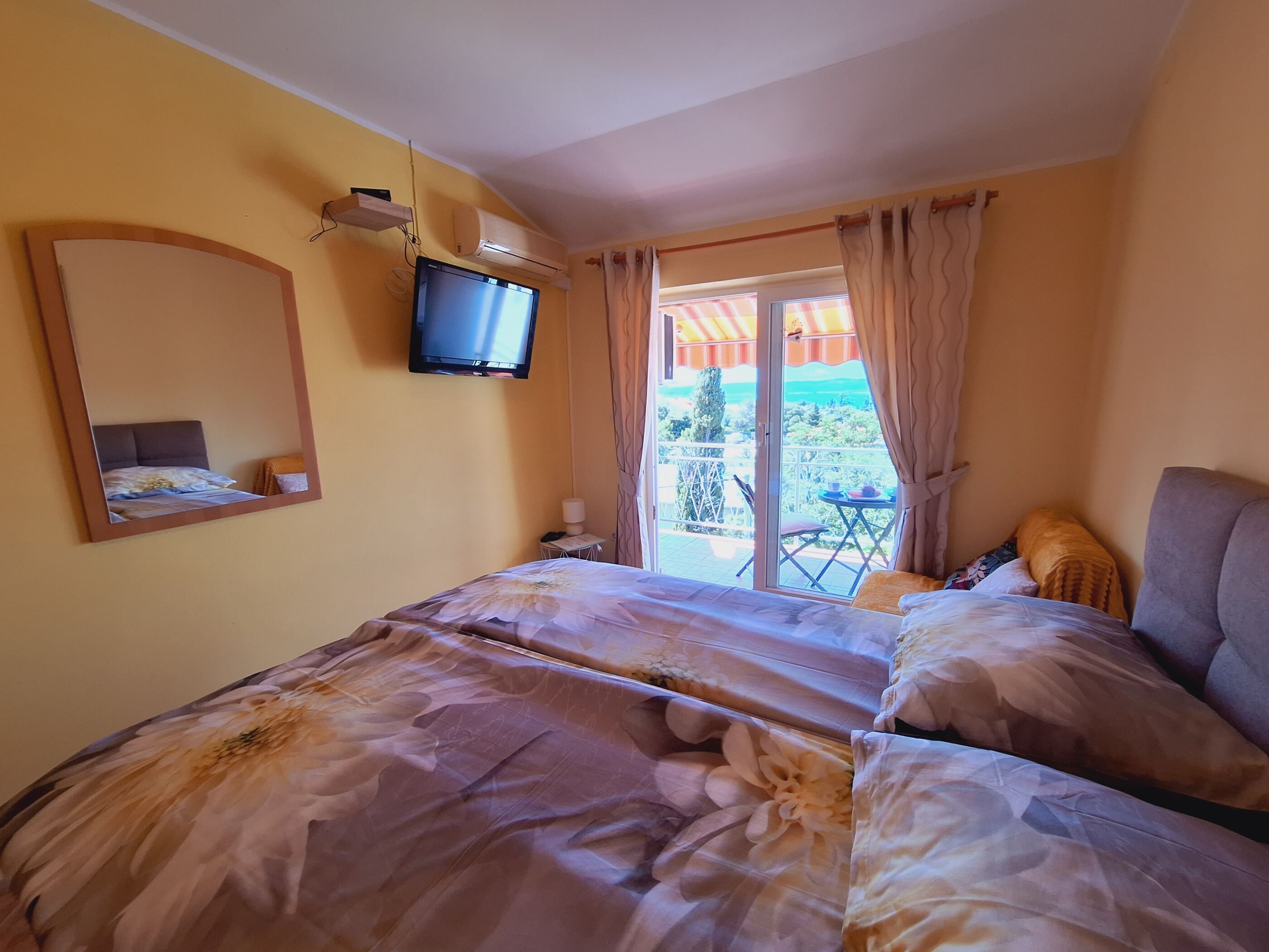 A hotel room with a bed, a television, a balcony with a table and chairs, and a view of the outdoors.