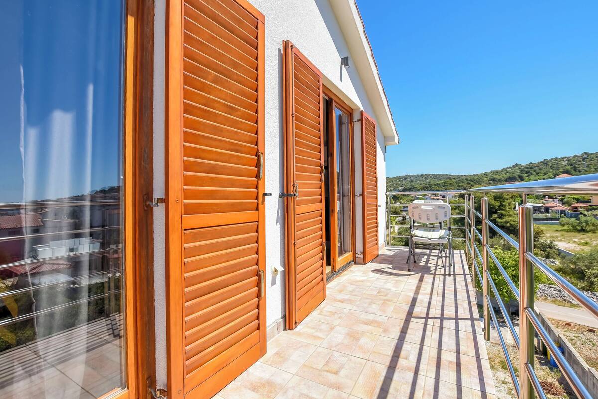 A balcony with wooden shutters, a chair, and a view of the landscape.
