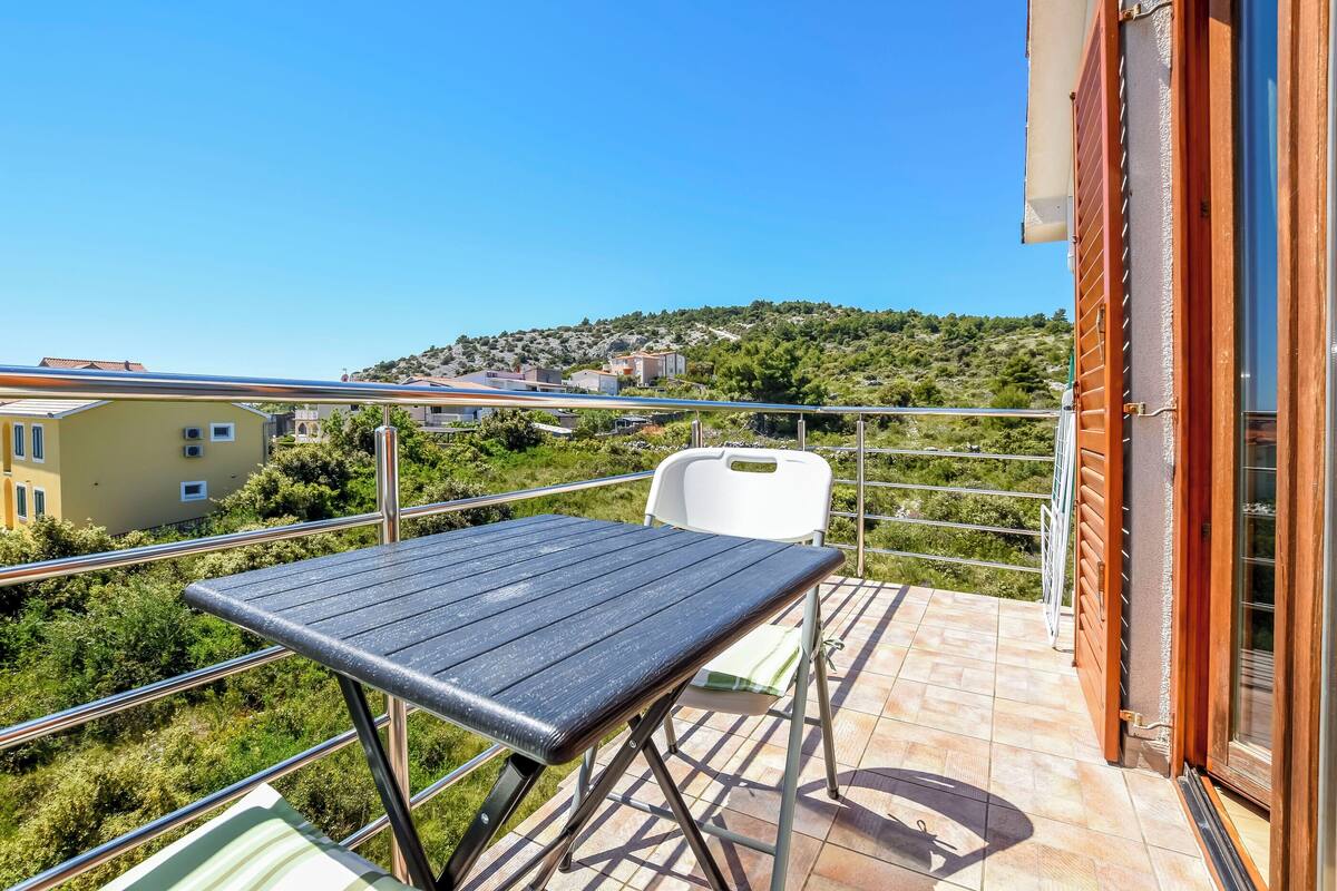 A balcony with a table and chairs, overlooking a hillside with buildings.