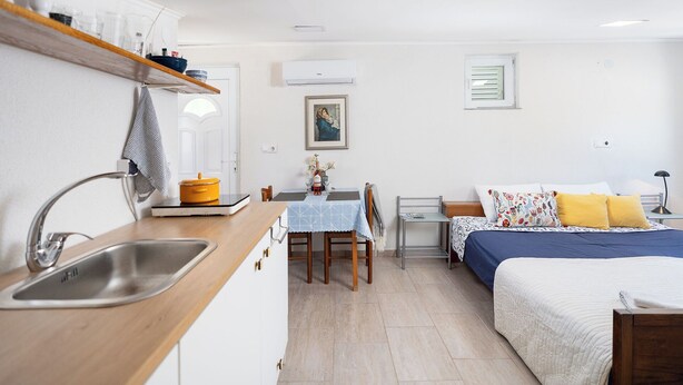Une cuisine compacte comprenant un évier, une table avec des chaises, un lit avec une couvre-lit bleue et jaune, et une petite table de chevet avec une lampe.