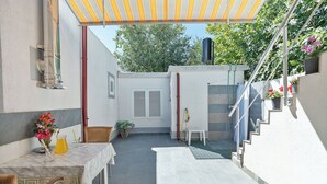 Un patio couvert avec une table et des chaises, un petit escalier et une porte donnant sur un espace extérieur abrité.