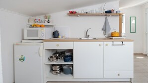 Une cuisine compacte équipée d’un four à micro-ondes, d’une bouilloire, d’un évier et de divers ustensiles rangés sur des étagères.