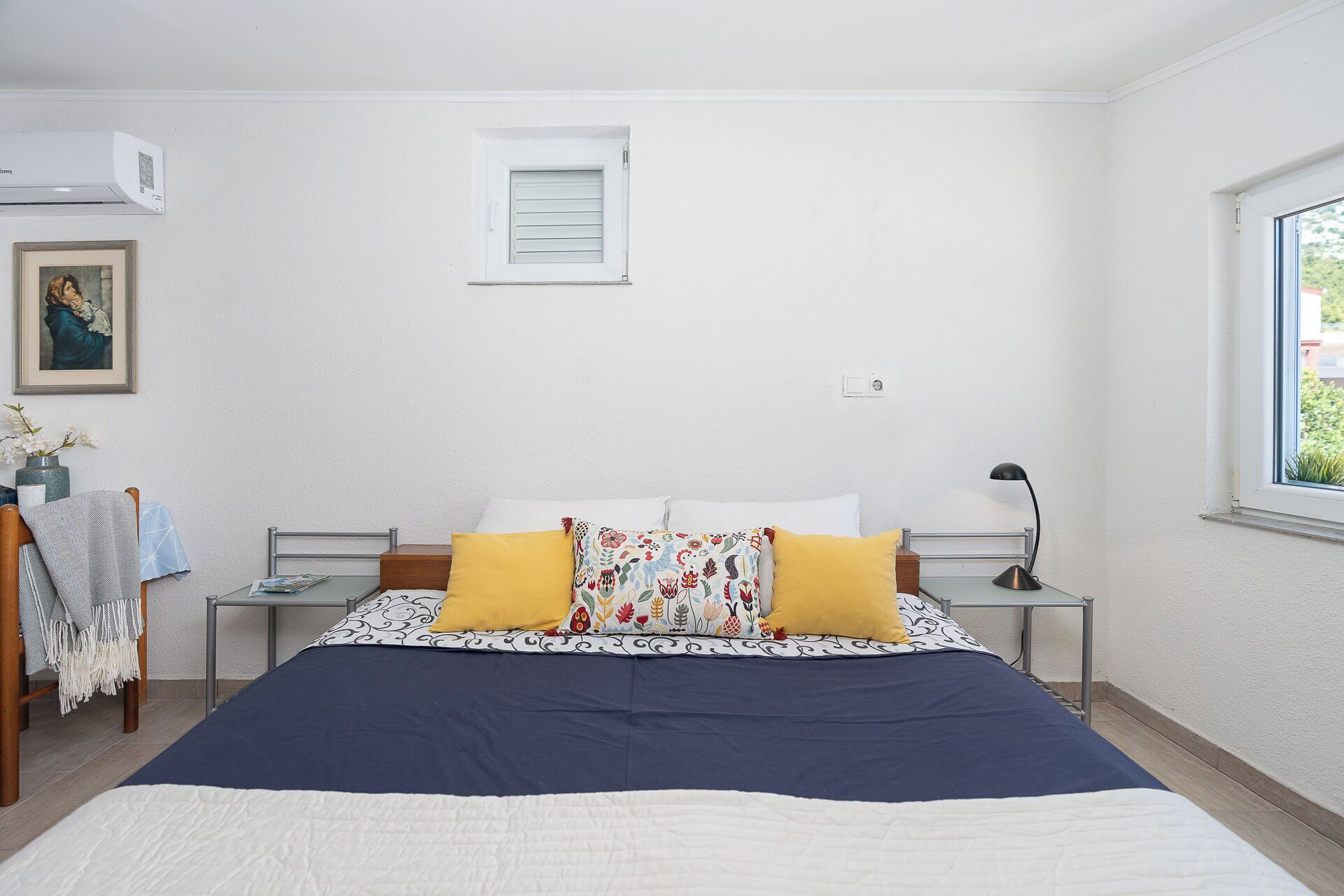 A bedroom with a bed, bedside tables, a window, and a painting on the wall.