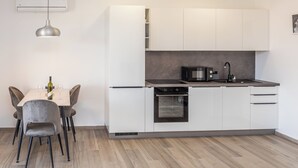 A modern kitchen with white cabinets, a built-in oven, and a dining area with a table and chairs. - Apartment Krtica (Vrbnik)