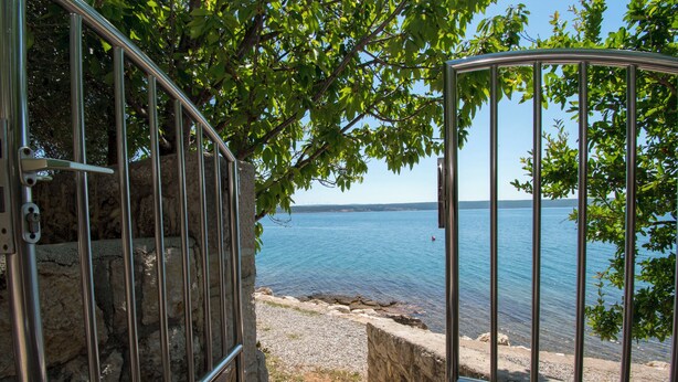 A metal gate leading to a rocky shoreline with a view of calm water and distant land. - Apartment Ana (Jasenice)