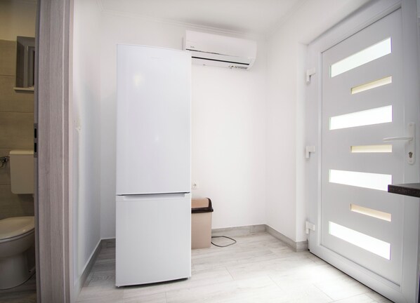 A compact kitchen with a white refrigerator, a built-in air conditioner, and a door with illuminated panels. - Apartment Ana (Jasenice)