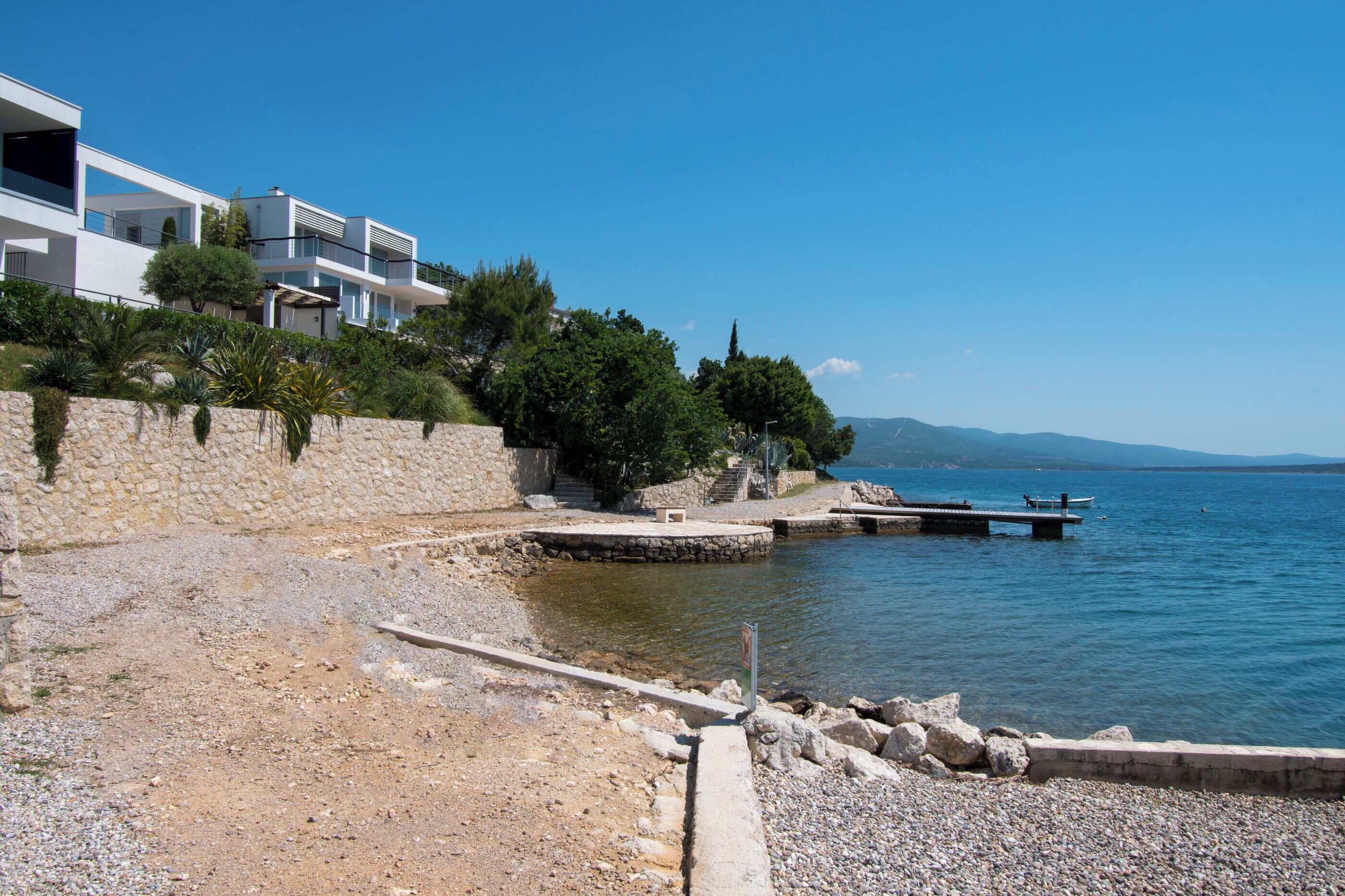 Une propriété située sur la côte, dotée d’un mur en pierre, d’une jetée en bois et offrant une vue dégagée sur la mer.