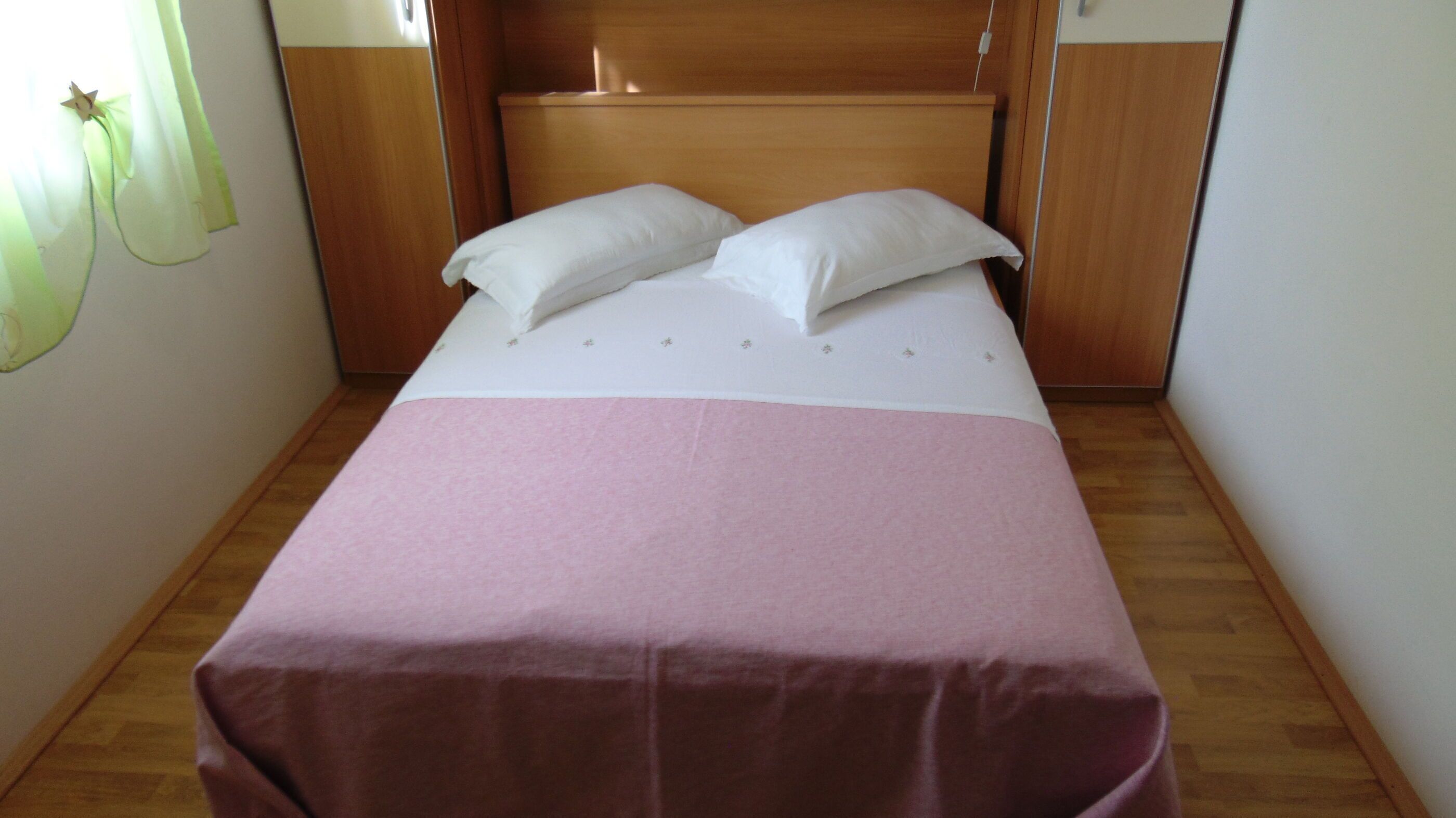 Un lit simple avec une couvre-lit rose et deux oreillers blancs, une tête de lit en bois et un plancher en bois.