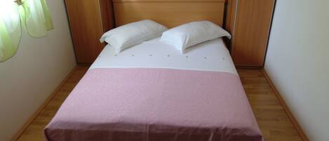 Un lit simple avec une couvre-lit rose et deux oreillers blancs, une tête de lit en bois et un plancher en bois.