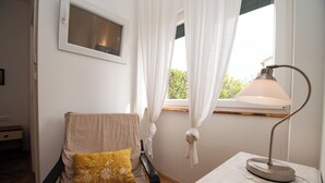 A room with a chair, a table with a lamp, a window with curtains, and a small window above the chair. - Apartment Nina (Rab)