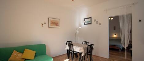 Une pièce avec un canapé vert, une table à manger avec des chaises, un ventilateur de plafond et un lit à baldaquin.