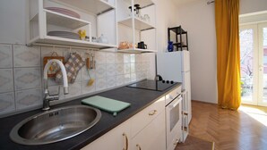 A kitchen with a sink, stove, and cabinets, a window with yellow curtains, and a tiled backsplash. - Apartment Nina (Rab)