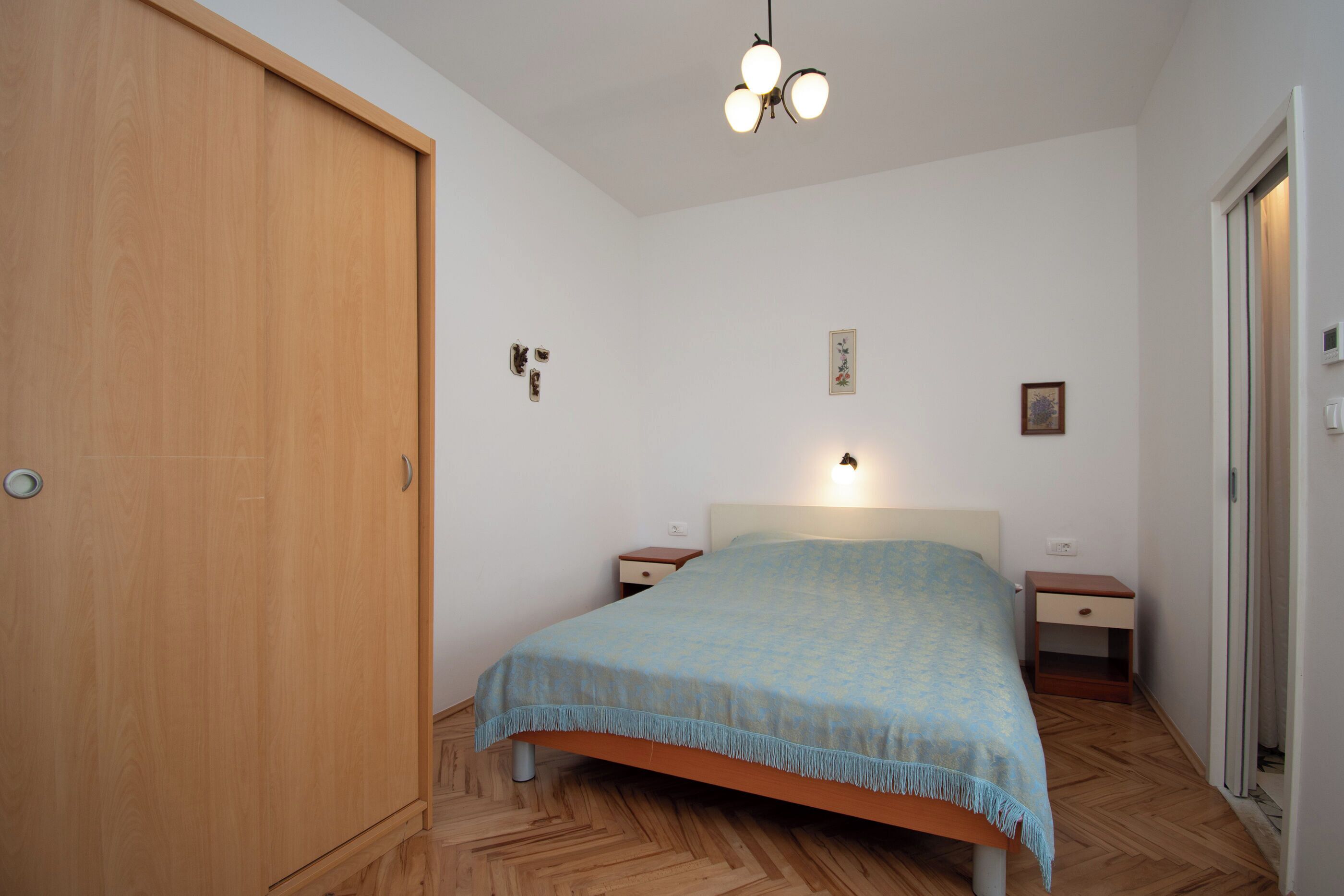A bedroom with a bed, wooden wardrobe, bedside tables, and a ceiling light fixture.