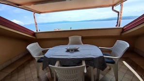 Ein kleiner Balkon mit Tisch und Stühlen, der auf ein Gewässer und ferne Berge blickt.
