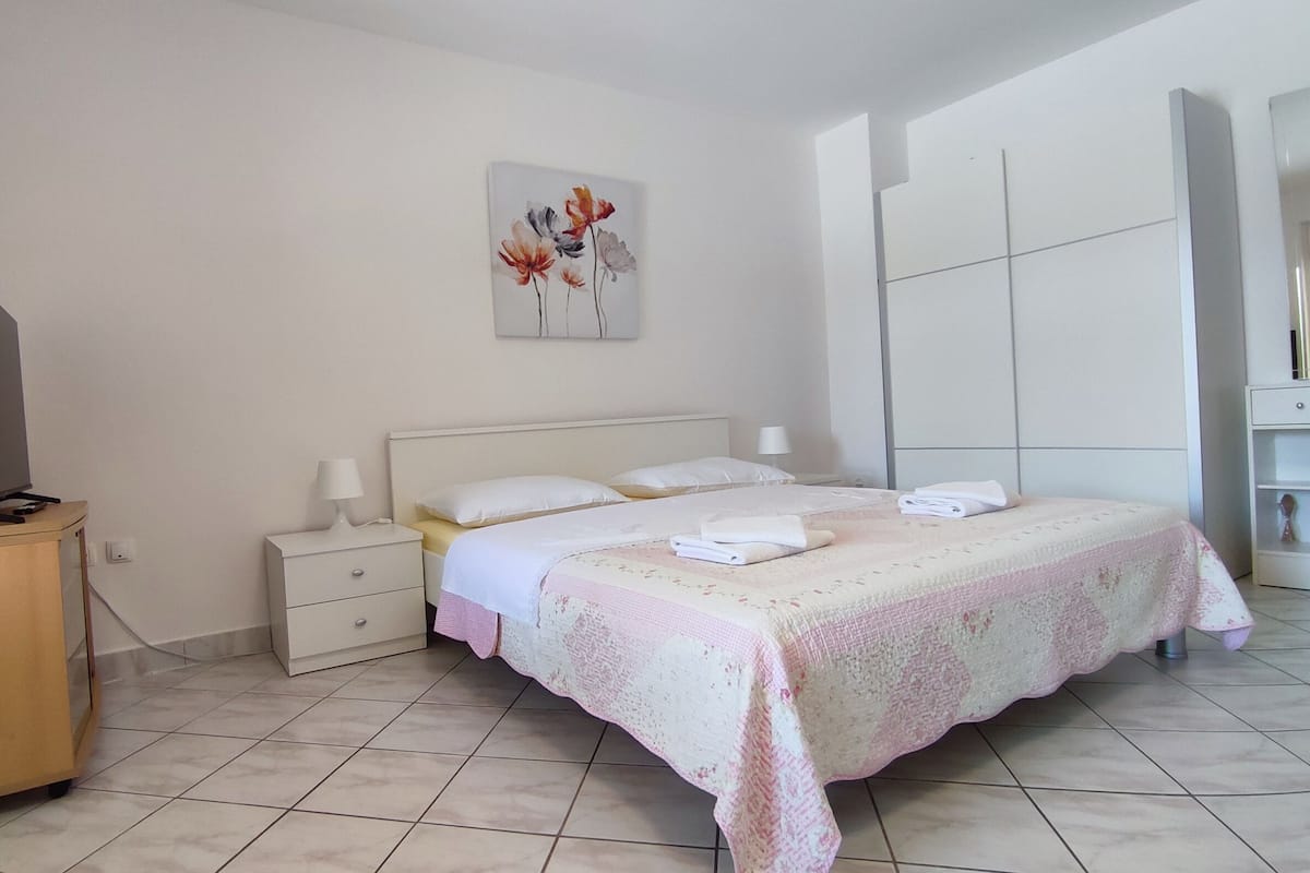 A bedroom with a bed, a nightstand, a TV on a stand, and a painting on the wall.