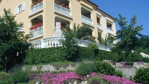 Un hôtel à plusieurs étages doté de balcons, entouré de jardins aménagés et de plantes en fleurs.