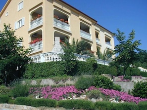 Ein mehrstöckiges Hotel mit Balkonen, umgeben von üppiger Vegetation und blühenden Pflanzen.