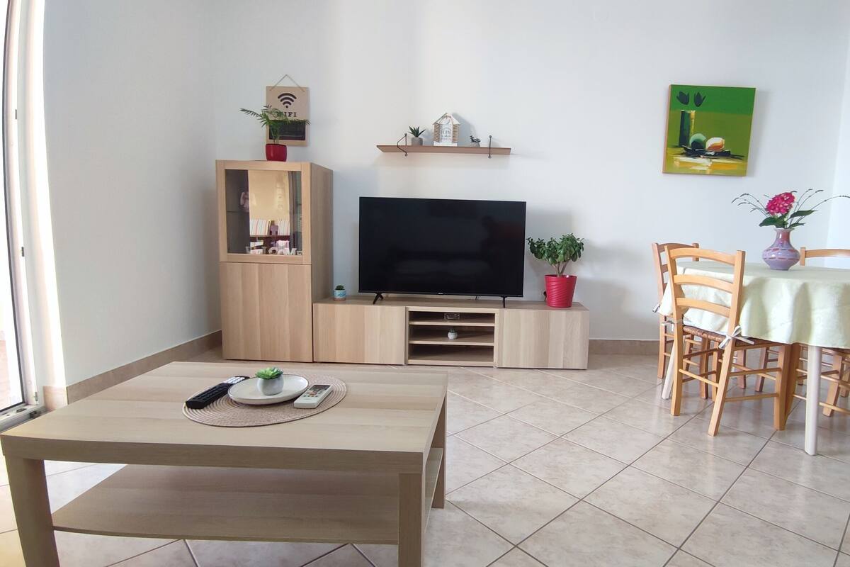 A living room with a TV, wooden furniture, a dining table, and a small plant.