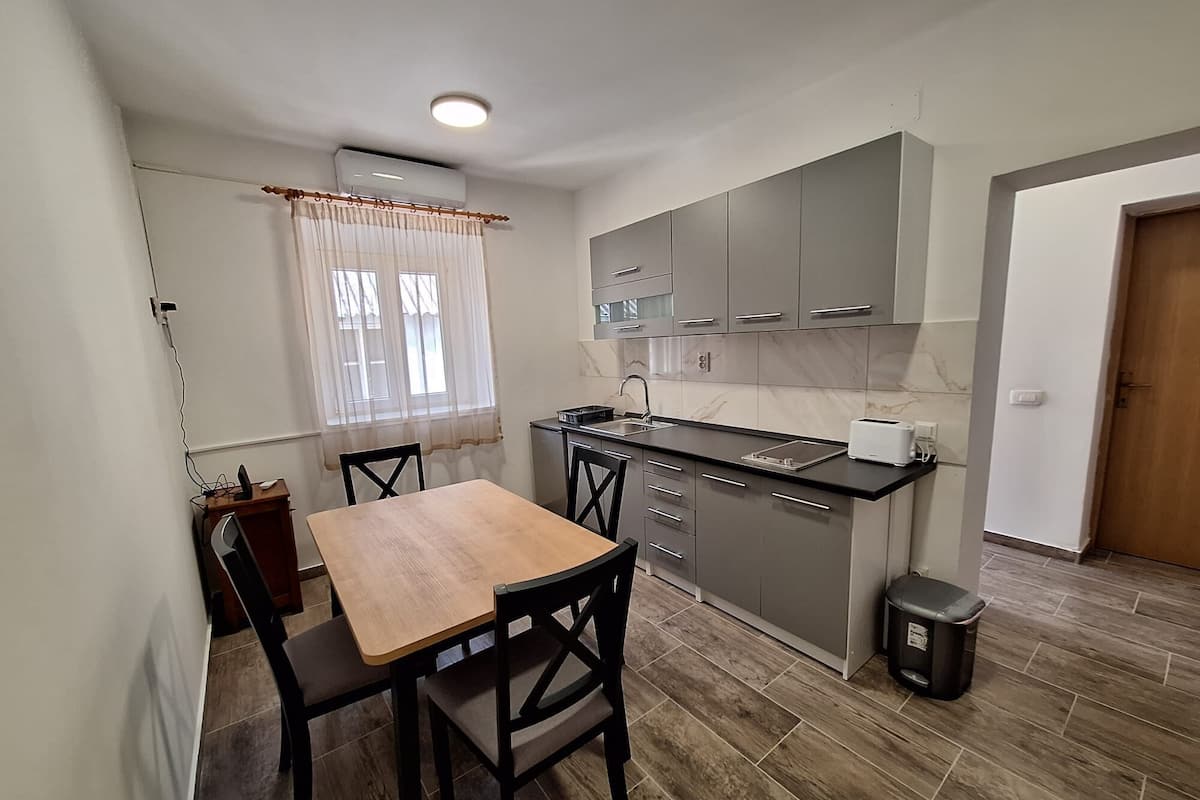 A compact kitchen with a dining area, including a wooden table and chairs, a built-in oven, and a trash bin.