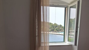 Un dormitorio con una cama, una ventana que ofrece vistas a un cuerpo de agua y vegetación, y una cortina.