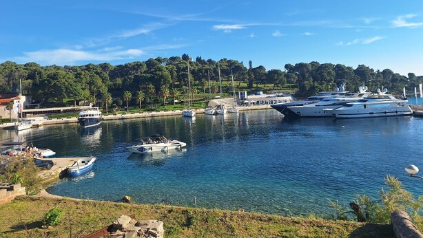 Un puerto deportivo con varios yates amarrados, un bote pequeño y un edificio con tejado rojo.