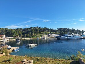 A marina with several yachts docked, a small boat, and a building with a red roof. - Apartments Neptun (Solta)