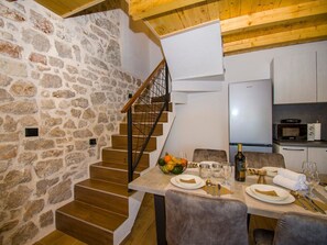 Comedor con pared de piedra, escalera de madera y cocina equipada con electrodomésticos modernos.