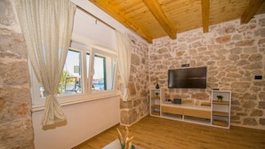 A cozy room with stone walls, a wooden ceiling, a TV mounted on the wall, and a wooden floor. - House Olivera (Tribunj)