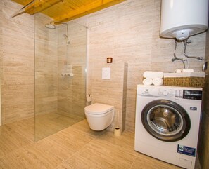 Un baño con ducha de vidrio, inodoro y lavadora de carga frontal.
