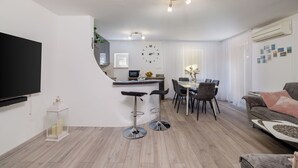 A modern living room with a flat-screen TV, two bar stools, a dining area with a table and chairs, and a sofa. - Apartment Lokvica (Omisalj)