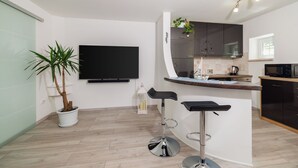 A modern kitchen with a flat-screen TV, a bar area with stools, and a potted plant. - Apartment Lokvica (Omisalj)