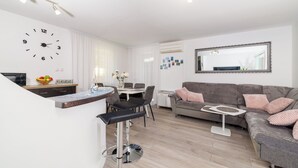 A modern living room with a grey sofa, a round coffee table, and a dining area with a white table and chairs. - Apartment Lokvica (Omisalj)