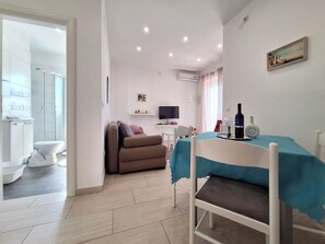 Ein modernes Wohnzimmer mit einer Couch, einem Esstisch mit blauer Tischdecke, einem Fernseher und einem Bild an der Wand.
